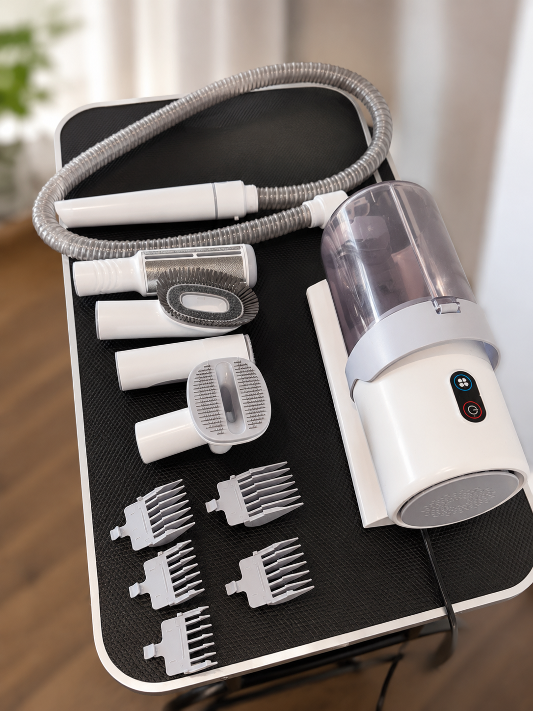 A cordless grooming kit with a white and gray handheld device, a flexible hose, multiple white attachment heads, and six gray comb guards, displayed on a black textured tray.
