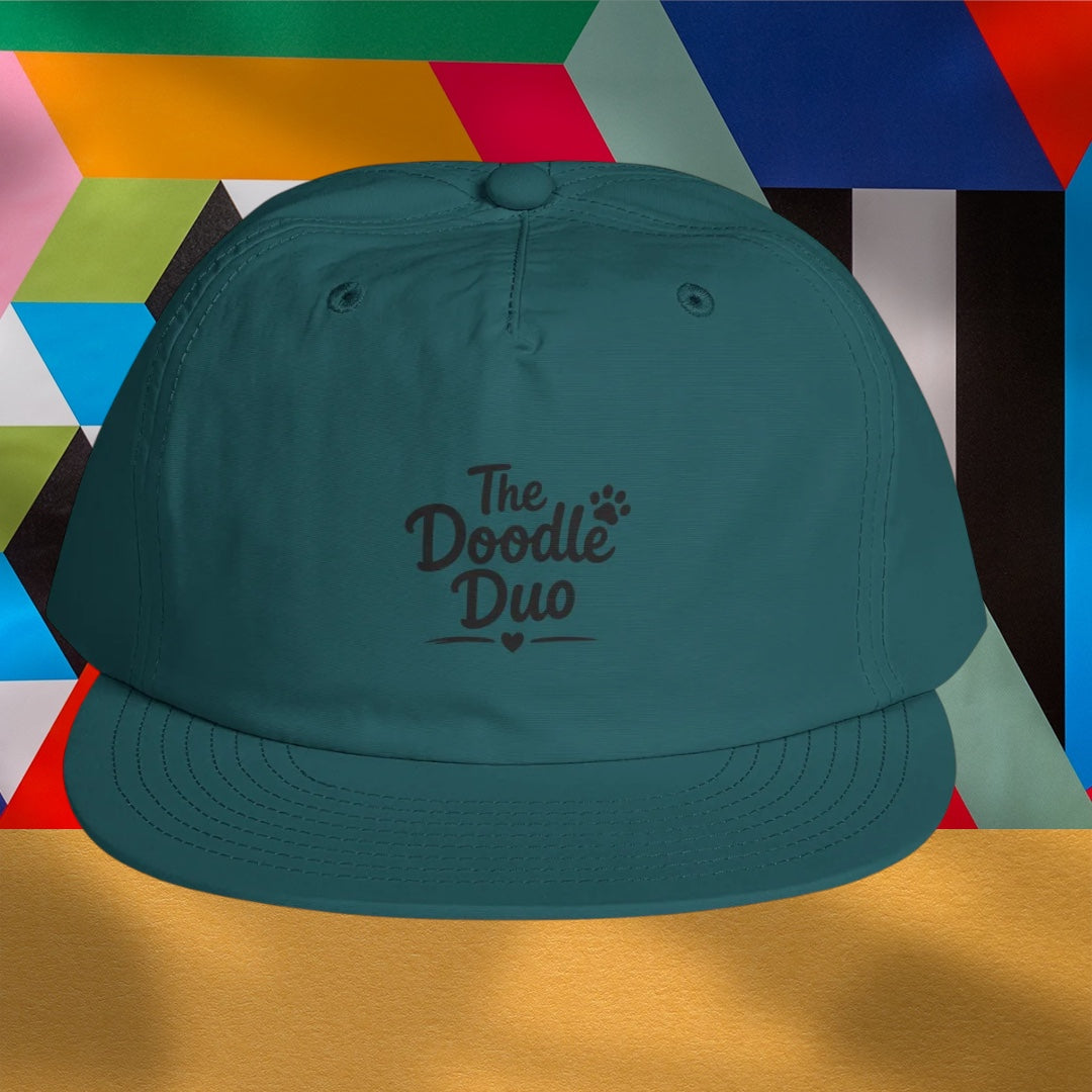 A teal baseball cap with 'The Doodle Duo' and a paw print logo on the front, set against a colorful geometric background.