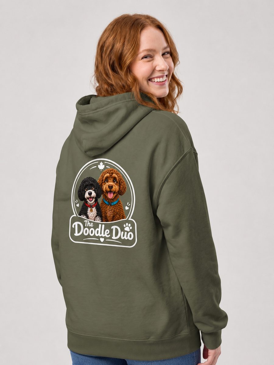 A woman with red hair is shown from the back wearing an olive green hoodie. The hoodie features a large graphic print on the back depicting two dogs inside an oval frame with the text 'The Doodle Duo'.