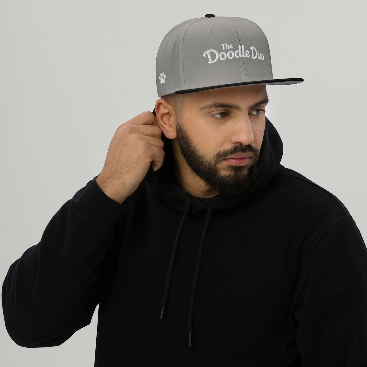 A man wearing The Doodle Duo grey snapback hat with white signature wordmark and paw embroidery on a black hoodie.