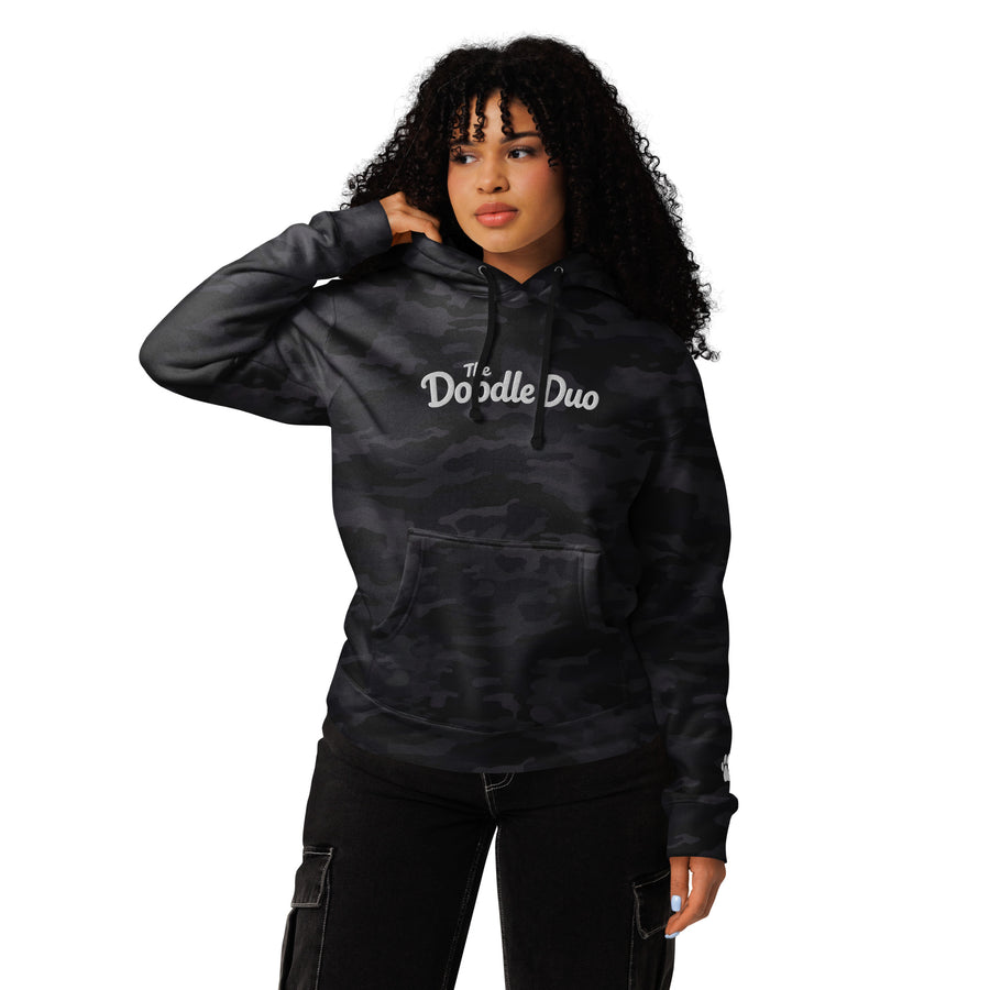 Person wearing a black camouflage hoodie with a logo on a white background